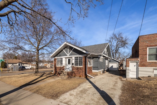 bungalow featuring an outbuilding, brick siding, roof with shingles, and driveway