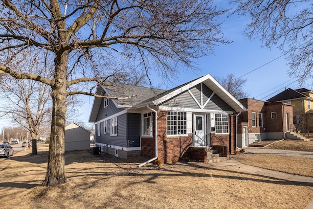 view of front of home featuring brick siding, cooling unit, a shingled roof, and an outdoor structure