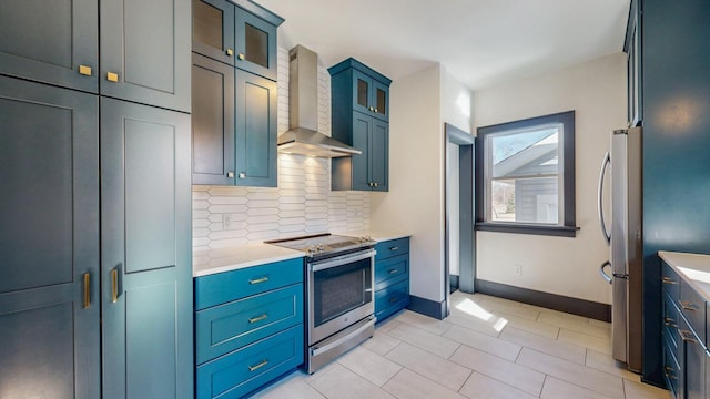 kitchen with baseboards, glass insert cabinets, appliances with stainless steel finishes, wall chimney range hood, and backsplash