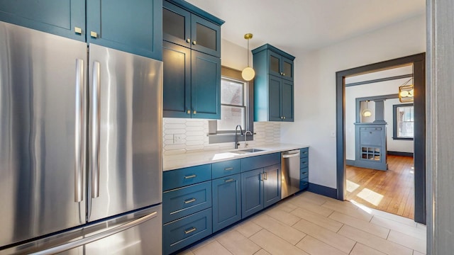 kitchen featuring blue cabinetry, light countertops, decorative backsplash, appliances with stainless steel finishes, and a sink