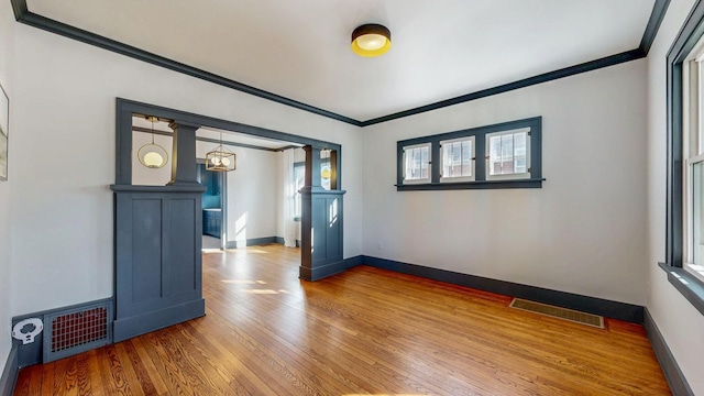 empty room featuring hardwood / wood-style floors, crown molding, decorative columns, and visible vents