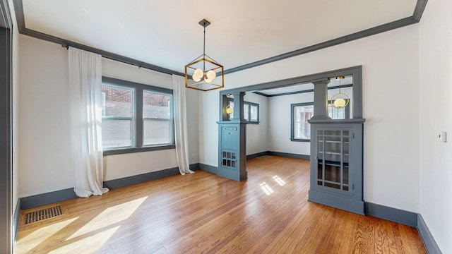 unfurnished dining area with visible vents, ornamental molding, wood finished floors, a chandelier, and ornate columns