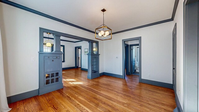 empty room with decorative columns, wood finished floors, baseboards, and ornamental molding