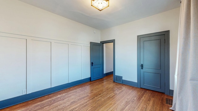 unfurnished bedroom featuring visible vents, a decorative wall, and wood finished floors