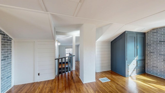 bonus room featuring vaulted ceiling, wood finished floors, visible vents, and brick wall