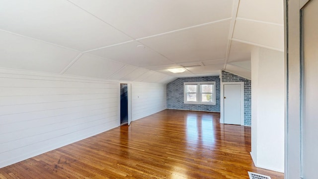 additional living space featuring vaulted ceiling, wood finished floors, visible vents, and brick wall