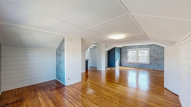 bonus room with hardwood / wood-style floors, brick wall, and vaulted ceiling