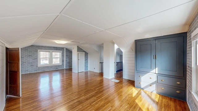 bonus room with light wood finished floors, visible vents, brick wall, and vaulted ceiling