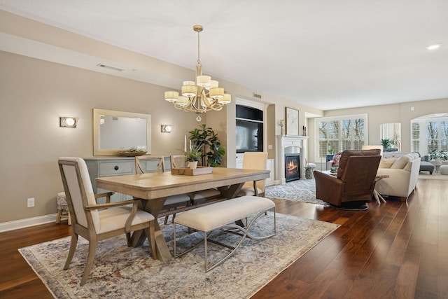 dining space with baseboards, visible vents, dark wood-type flooring, a glass covered fireplace, and a notable chandelier