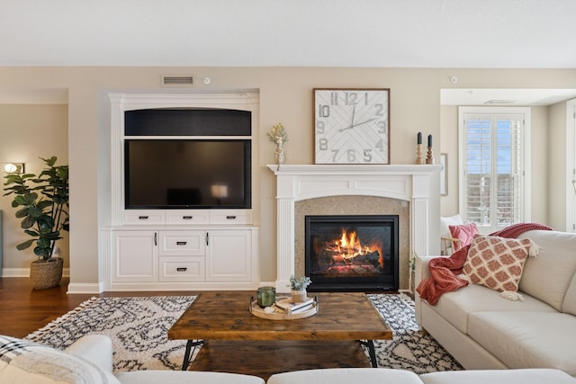 living area with a glass covered fireplace, wood finished floors, visible vents, and baseboards