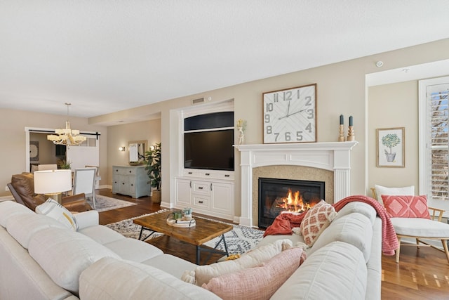 living area featuring visible vents, baseboards, a chandelier, wood finished floors, and a glass covered fireplace