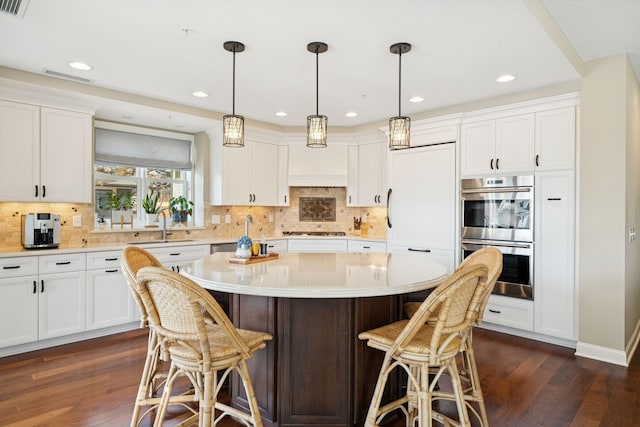 kitchen with gas cooktop, double oven, a breakfast bar, and dark wood-type flooring