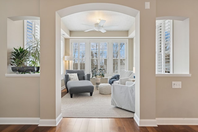 sitting room featuring arched walkways, baseboards, a ceiling fan, and wood finished floors