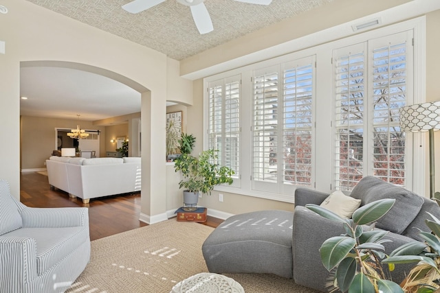 living room featuring visible vents, baseboards, ceiling fan with notable chandelier, wood finished floors, and arched walkways