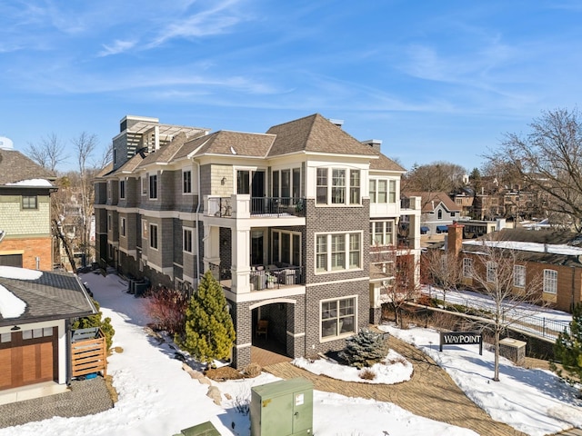 snow covered back of property featuring brick siding and a balcony