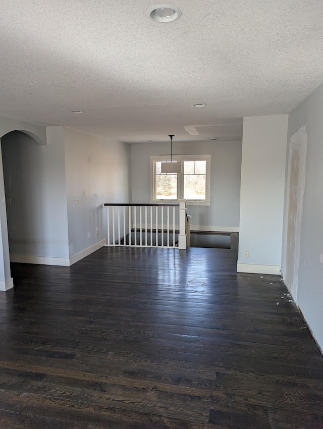 empty room featuring dark wood-style floors, arched walkways, a textured ceiling, and baseboards