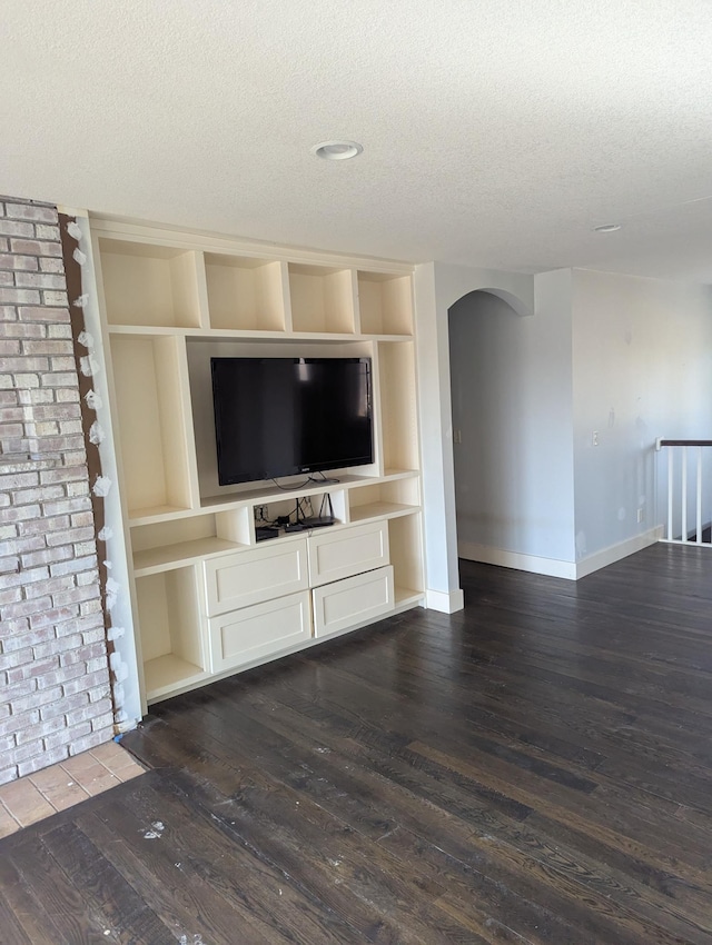 unfurnished living room featuring baseboards, built in features, arched walkways, a textured ceiling, and dark wood-style flooring