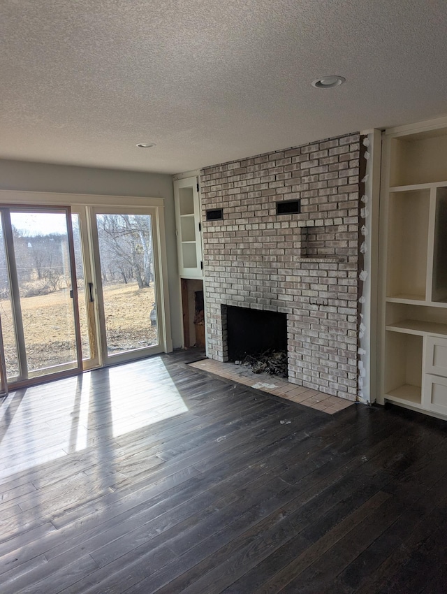 unfurnished living room featuring built in shelves, a textured ceiling, wood finished floors, and a fireplace