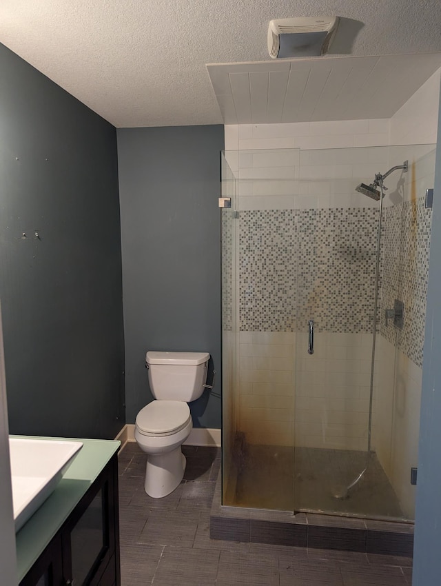 full bath with vanity, baseboards, a shower stall, a textured ceiling, and toilet