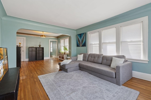 living room featuring arched walkways, plenty of natural light, and wood finished floors