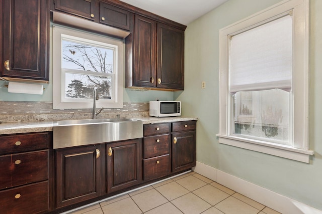 kitchen with a sink, white microwave, dark brown cabinetry, and light countertops