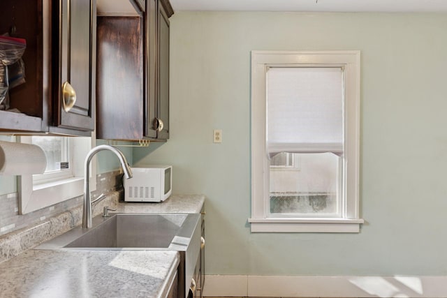 kitchen with white microwave, dark brown cabinets, light countertops, and a sink