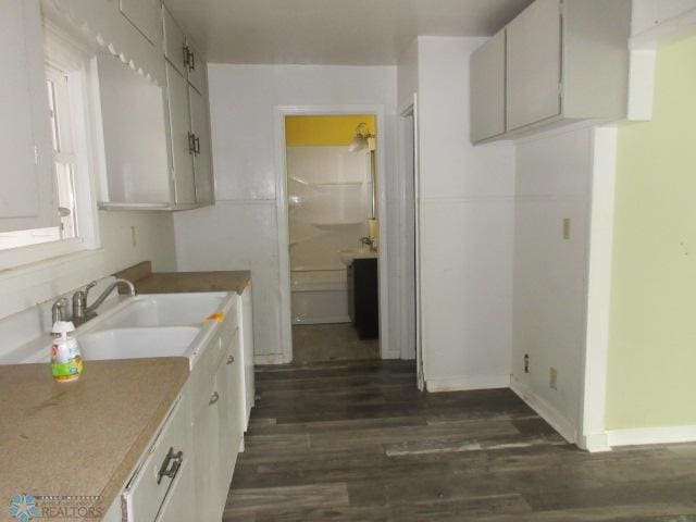 kitchen featuring dark wood finished floors, light countertops, baseboards, and a sink