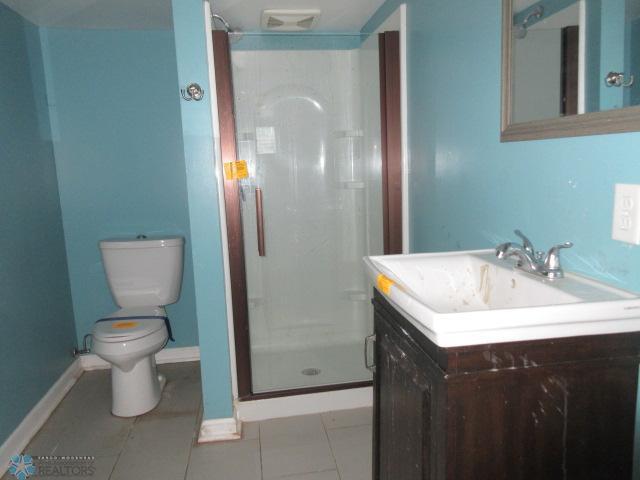 full bathroom with vanity, baseboards, a stall shower, tile patterned flooring, and toilet