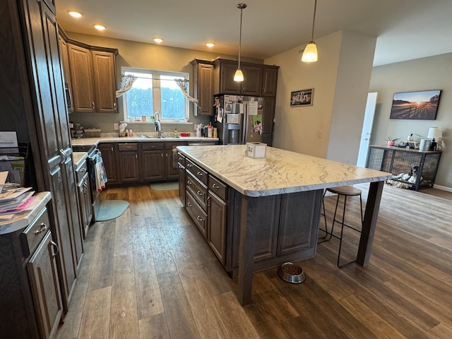 kitchen featuring dark wood-style floors, a breakfast bar, a sink, stainless steel refrigerator with ice dispenser, and a center island