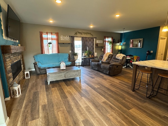 living room with recessed lighting, dark wood-type flooring, and a stone fireplace