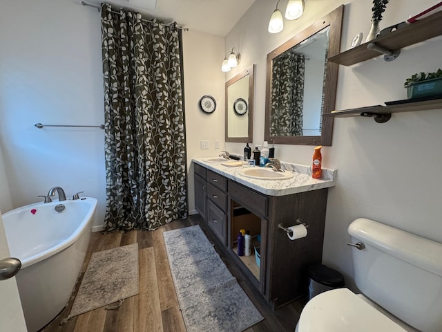 full bathroom featuring wood finished floors, double vanity, a freestanding tub, a sink, and toilet