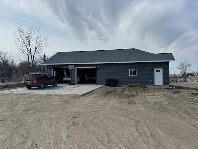 back of property featuring an outbuilding, driveway, a shingled roof, and a garage