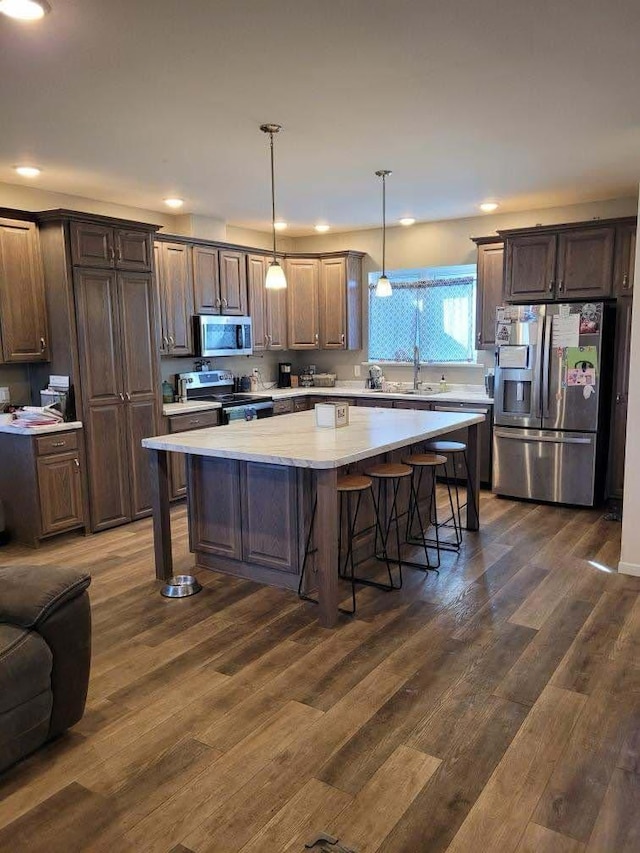 kitchen featuring stainless steel appliances, dark wood-type flooring, light countertops, a kitchen bar, and a center island