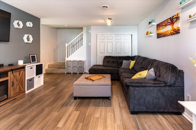 living area with visible vents, a textured ceiling, stairs, and wood finished floors