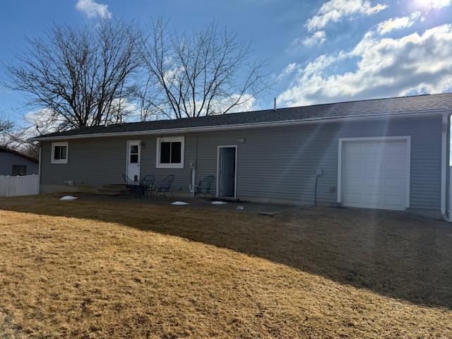 rear view of property featuring fence, a lawn, an attached garage, and entry steps