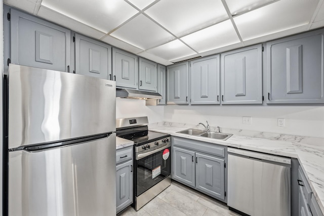 kitchen featuring light stone counters, gray cabinets, a sink, stainless steel appliances, and under cabinet range hood