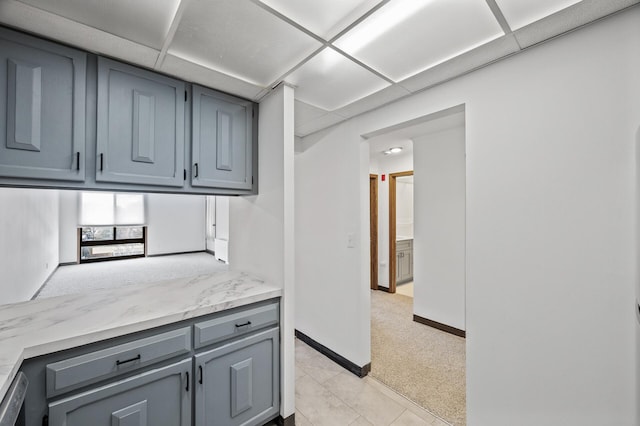 kitchen featuring light carpet, gray cabinets, a paneled ceiling, and baseboards