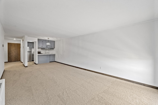 unfurnished living room featuring light colored carpet, an inviting chandelier, and baseboards