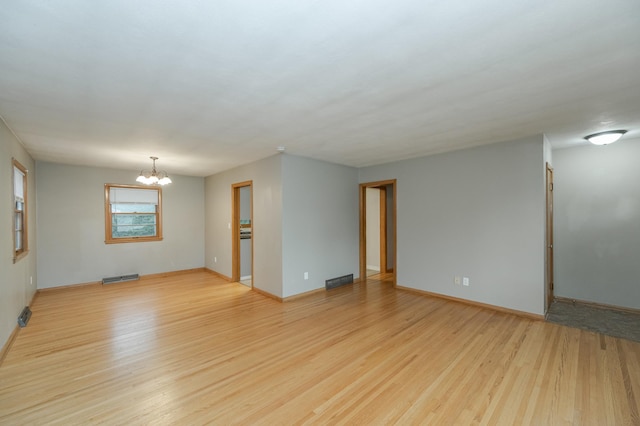 spare room with a notable chandelier, visible vents, light wood-type flooring, and baseboards