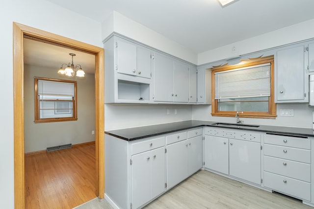 kitchen featuring dark countertops, light wood-style floors, visible vents, and a sink