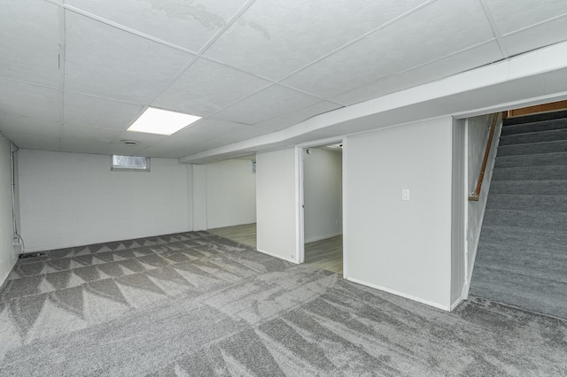 finished basement featuring carpet flooring, a paneled ceiling, concrete block wall, and stairs