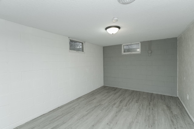 finished basement with a textured ceiling, light wood-style flooring, and concrete block wall