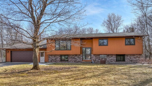 raised ranch featuring driveway, an attached garage, a front yard, brick siding, and a chimney