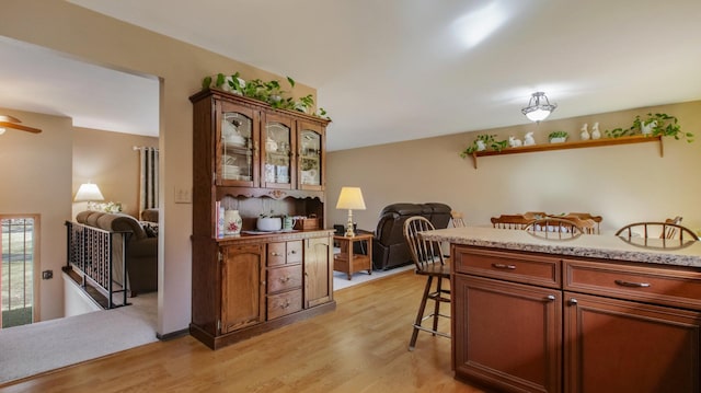 kitchen with light wood finished floors, open floor plan, glass insert cabinets, and a kitchen bar