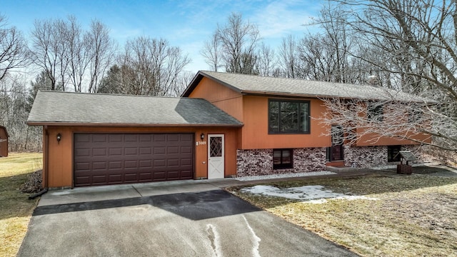 split level home featuring an attached garage, brick siding, driveway, and roof with shingles