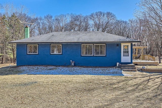back of house with a shingled roof, stucco siding, a deck, and a yard