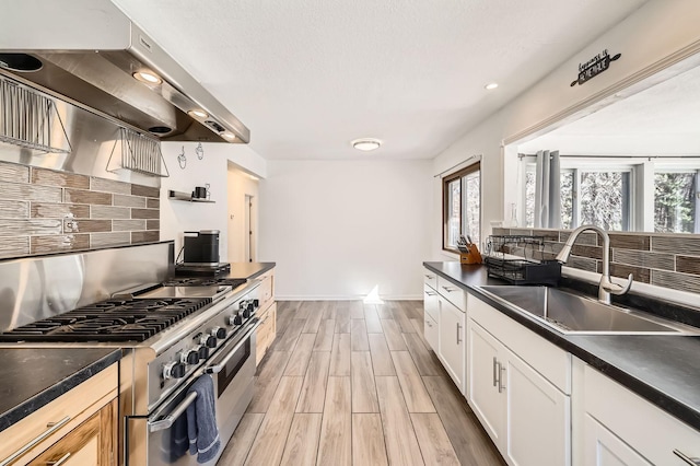 kitchen with dark countertops, a sink, double oven range, and under cabinet range hood
