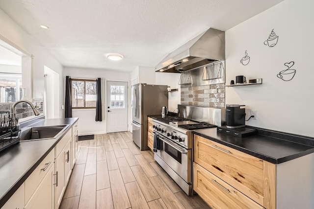 kitchen featuring a sink, wall chimney exhaust hood, appliances with stainless steel finishes, dark countertops, and decorative backsplash