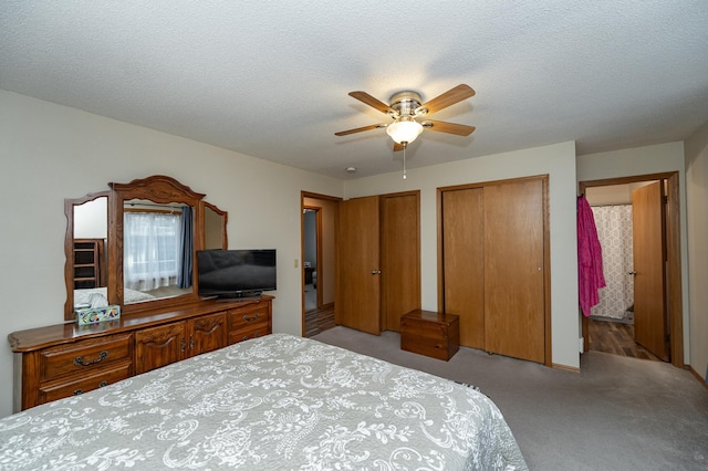 carpeted bedroom with connected bathroom, two closets, a ceiling fan, and a textured ceiling