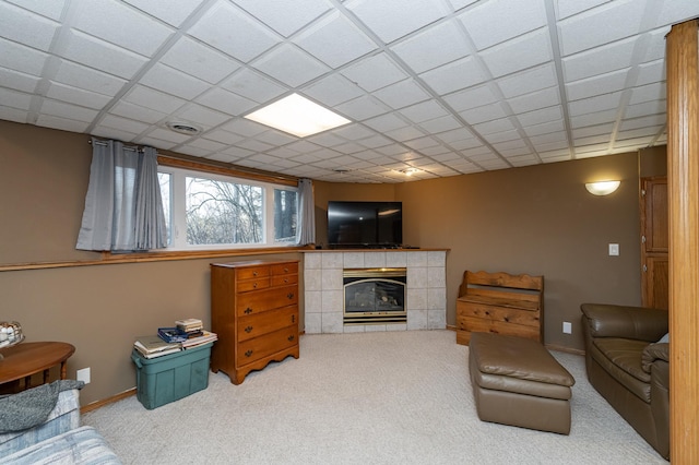 carpeted living area with a tiled fireplace, visible vents, a paneled ceiling, and baseboards